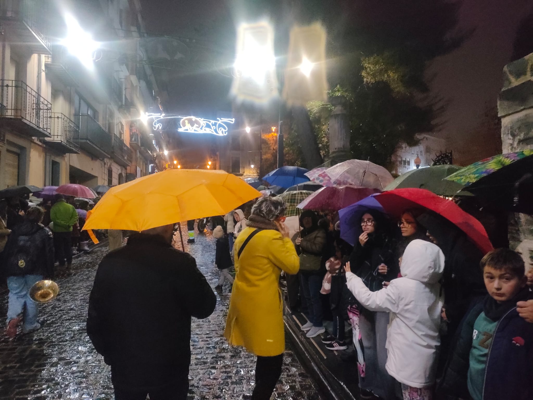 Molta gent al carrer, tots amb paraigües, esperant l'arribada de l'Ambaixador Reial. 